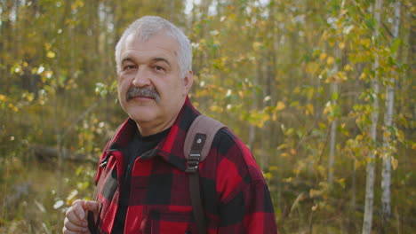 portrait-of-grey-haired-tourist-with-moustache-in-forest-at-autumn-day-man-is-smiling-to-camera-ecotourism
