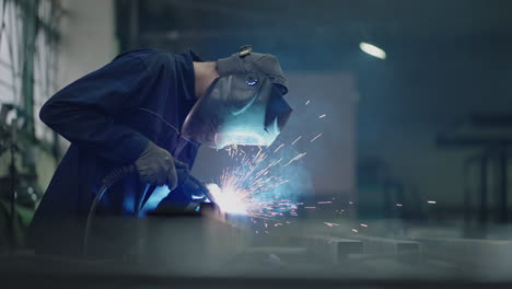 A-male-welder-works-in-a-factory-and-welds-steel-metal-parts-in-slow-motion.-Sparks-fly