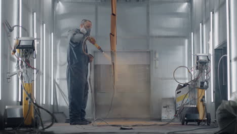A-man-in-a-protective-suit-and-mask-sprays-paint-through-a-spray-gun-in-slow-motion-on-steel-parts.