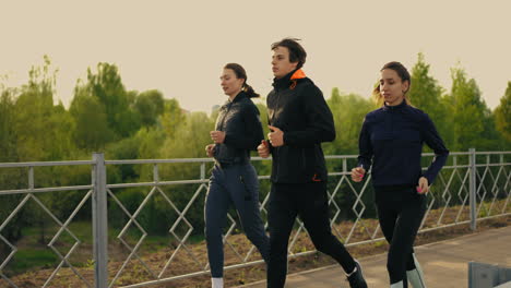 Tres-Jóvenes-Corren-Sobre-Un-Puente-En-Una-Mañana-De-Verano-Entrenando-Juntos-Para-Mantenerse-En-Forma