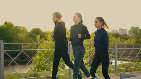 Gruppe-Von-Drei-Läufern-Beim-Morgendlichen-Joggen-Zwei-Weibliche-Und-Ein-Männlicher-Sportler-Laufen-Gemeinsam-Am-Stadtrand