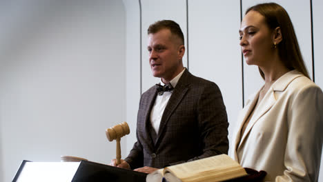 Man-in-elegant-suit-with-gavel-and-woman-holding-book
