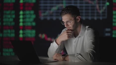 A-professional-with-glasses-looks-at-the-computer-monitor-screen-and-thinks-analyzing-the-securities-market.-Brooding-puzzled-broker-waits-for-the-growth-of-shares