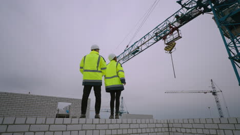 two-civil-engineers-are-viewing-construction-site-male-and-female-figures-against-building-crane