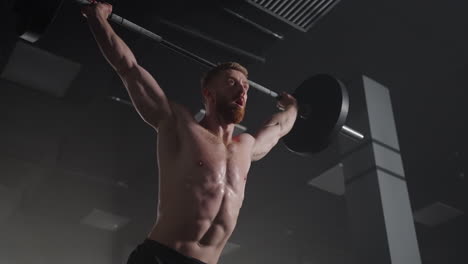 Slow-motion:-Brutal-athlete-lifts-the-bar-above-himself-performing-a-jerk-a-spinning-push.-A-man-is-engaged-in-weightlifting-on-a-dark-background-portrait.-Concept-strength-power-playing-sports.