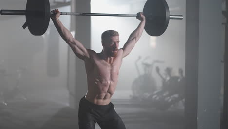 Slow-motion:-Brutal-athlete-lifts-the-bar-above-himself-performing-a-jerk-a-spinning-push.-A-man-is-engaged-in-weightlifting-on-a-dark-background-portrait.-Concept-strength-power-playing-sports.