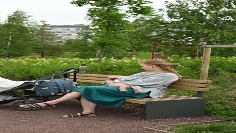 Woman-with-baby-and-stroller-sitting-in-bench-in-park