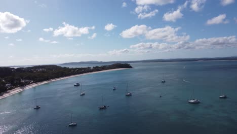 Drone-flying-over-sailing-boats-towards-a-white-sandy-beach