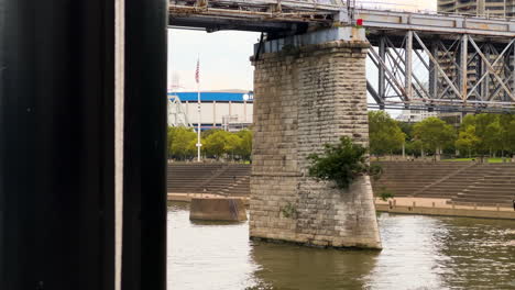 Ohio-River-Cruise-Crossing-Under-Purple-People-Bridge-Near-Serpentine-Wall-Park-In-Newport,-Kentucky,-USA