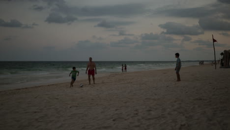 Dad-playing-football-soccer-with-his-kids-in-a-white-sand-beach-with-crystal-clear-ocean-in-Cancun,-Mexico