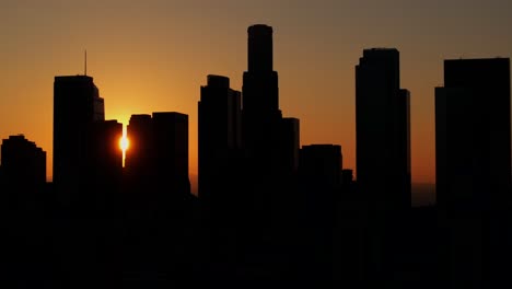 Downtown-Los-Angeles,-California-skyline-silhouetted-cinematic-sunset---rising-aerial