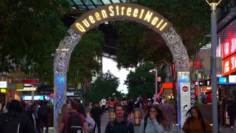 Static-shot-capturing-people-shopping-and-dinning-at-bustling-Queen-street-mall-on-a-Friday-night,-large-crowds-in-downtown-Brisbane-city-with-light-up-landmark-archway-sign-at-Albert-street