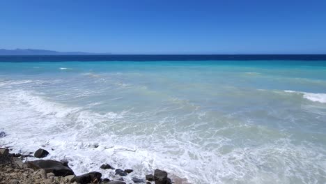 Ruhige-Mediterrane-Gelassenheit:-Azurblaues-Meer-Und-Weiße-Wellen-Plätschern-Sanft-An-Der-Felsigen-Küste-Eines-Ruhigen,-Abgeschiedenen-Strandes