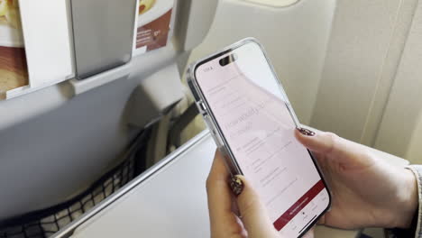 Schwenk-Vom-Flugzeugfenster-Zur-Kaukasischen-Reisendenin,-Die-Am-13.07.2023-In-Einem-Westjet-Flugzeug-Durch-Die-Westjet-App-Scrollt,-Ohne-Internetverbindung-Am-Flughafen-Lax