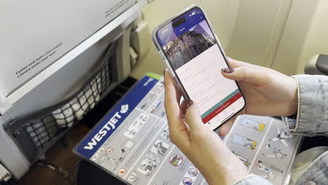 Caucasian-Woman-Traveler-Scrolling-Through-WestJet-Flight-Details-on-Cellphone-on-WestJet-Airplane,-at-LAX-Airport-on-7-13-2023