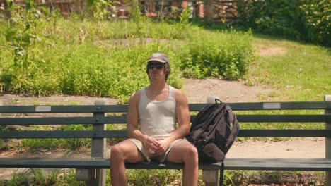 Man-scratches-face-looks-around-relaxing-on-park-bench-in-central-park-new-york