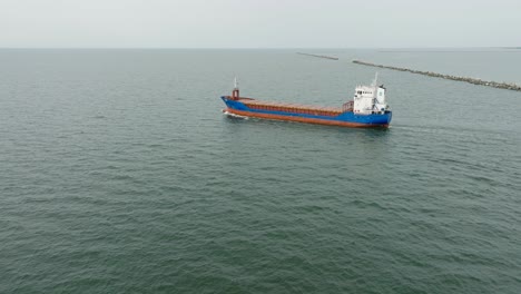 Aerial-establishing-view-of-large-blue-cargo-ship-leaving-Port-of-Liepaja-,-Karosta-bridge,-slight-overcast-day,-calm-Baltic-sea,-wide-drone-dolly-shot-moving-left