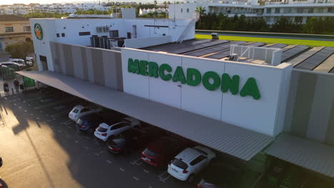 Aerial-view-of-Mercadona-grocery-store-parking-with-solar-panels-on-the-rooftop,-green-energy-business-in-Marbella-Estepona-Malaga-Spain,-people-shopping-at-a-Spanish-supermarket,-4K-static-shot