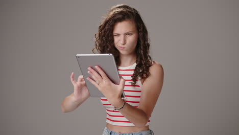 Brunette-girl-uses-tablet,-smiles-and-nods,-half-body-studio-shot