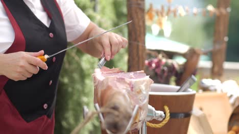 female-slicing-prosciutto-on-table-outdoors,-detail-shot-of-woman-cutting-raw-meat
