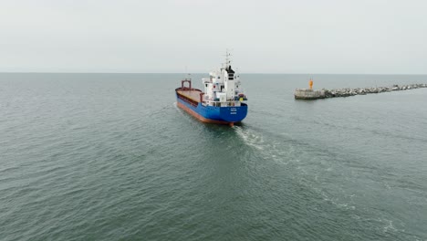 Aerial-establishing-view-of-large-blue-cargo-ship-leaving-Port-of-Liepaja-,-Karosta-bridge,-slight-overcast-day,-calm-Baltic-sea,-wide-drone-shot-moving-forward