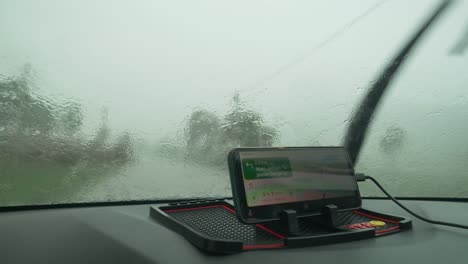Car-driving-in-heavy-rain-with-less-visibility,-WIndshield-wiper-cleaning-the-glass,-Driver-using-Google-map-for-road-direction-assistance
