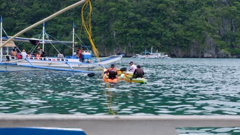 Grupo-De-Kayakistas-Vendiendo-Bebidas-Frías-Y-Cocos-A-Turistas-En-Barcos-Turísticos-De-Isla-En-Isla-En-El-Nido,-Palawan,-Filipinas