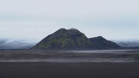 Wide-shot-of-Icelandic-landscape-with-mountains-and-flying-dust-over-field-in-wind