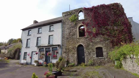 Colourful-Shopfront-joined-to-ancient-ruined-castle-covered-in-red-ivy-in-Inistioge-Kilkenny-summer-in-Ireland