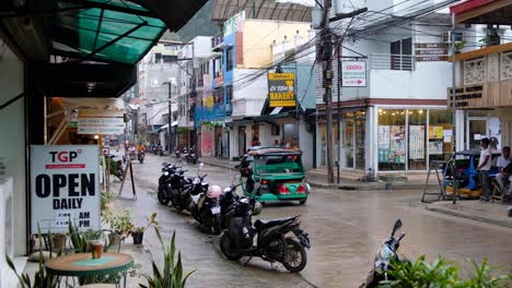 Vista-Panorámica-De-La-Calle-Con-Tiendas-Y-Cafés-Y-Tráfico-De-Triciclos-Y-Scooters-En-El-Nido,-Palawan,-Filipinas