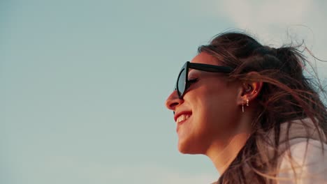 Zeitlupenaufnahme-Einer-Schönen-Frau-Mit-Sonnenbrille,-Die-Lächelt-Und-Den-Sonnenuntergang-Beobachtet