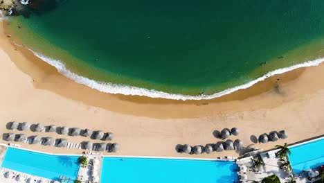 beach,-waves-and-ocean-topview-in-slowmotion,-Huatulco,-Mexico,-aerial-drone-descending,-zoom-in-to-beach-resort-with-swimming-pool