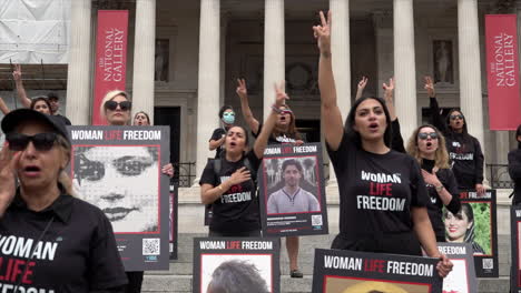 Demonstranten-Mit-Plakaten,-Auf-Denen-Mahsa-Amini-Und-Andere-Menschen-Abgebildet-Sind,-Die-Bei-Frauenrechtsprotesten-Im-Iran-Getötet-Wurden,-Stehen-Auf-Den-Stufen-Des-Trafalgar-Square-Und-Geben-Das-Friedenszeichen