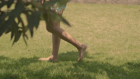Woman-in-Shorts-Walking-Barefoot-on-Grass-with-Green-Book-in-Hand,-Slow-Motion-Panning-Shot-in-the-Summer-Garden