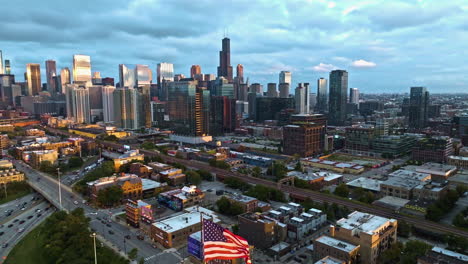 Waving-US-and-Chicago-Flag-in-front-of-the-sunrise-lit-West-Loop---Aerial-view