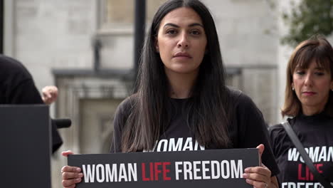 In-slow-motion-a-woman-holds-a-placard-that-reads,-“Woman-Life-Freedom”-during-a-protest-marking-the-death-of-Mahsa-Amini,-who-died-in-Iranian-police-custody-after-allegedly-violating-hijab-rules