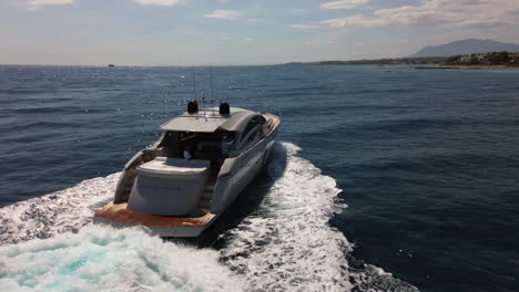 Aerial-view-of-following-a-luxury-yacht-driving-fast-in-sea,-sailing-in-Marbella-Spain,-beautiful-Mediterranian-sea,-jetset-elite-lifestyle,-4K-drone-shot