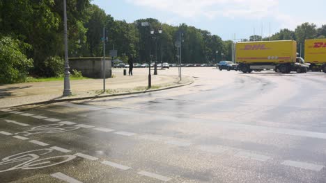 Car-crossing-a-road-next-to-a-park-with-trees-with-DHL-delivery-trucks