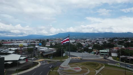 Drohne,-Die-Mitten-Im-Kreisverkehr-In-Richtung-Der-Costaricanischen-Flagge-Fliegt,-Mit-Schöner-Aussicht-Auf-Die-Berge-Im-Hintergrund
