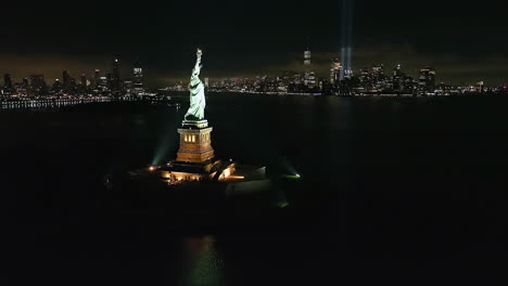 Eine-Luftaufnahme-Der-Freiheitsstatue-In-New-York-Bei-Nacht,-Mit-Dem-Tribut-In-Hellen,-Beleuchteten-Doppelstrahlen-Im-Hintergrund