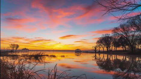 Fire-red-sunset-sky-lights-up-clouds-and-reflection-on-placid-lake,-golden-hour-time-lapse