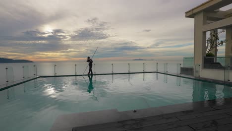 The-maintenance-man-cleaning-the-rooftop-pool-with-sunrise-in-background