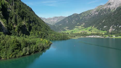 Unendliche-Berge-In-Der-Schweiz,-Bedeckt-Von-Der-Flora,-Bergfelsen,-Die-Hoch-In-Den-Himmel-Ragen,-Kleines-Dorf-Am-Ufer-Und-Ein-Boot,-Das-Auf-Dem-Meer-Segelt,-Perfekter-Ort-Für-Einen-Sonnigen-Kurzurlaub