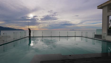 El-Hombre-De-Mantenimiento-Limpiando-La-Piscina-De-La-Azotea-Con-El-Amanecer-De-Fondo.