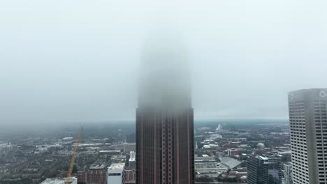Drone-shot-revealing-supertall-skyscraper-Bank-of-America-Plaza-through-the-clouds,-Peachtree-street-traffic,-Aerial-View