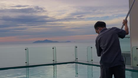 Close-up-the-maintenance-man-cleaning-the-rooftop-pool-with-sunrise-in-background