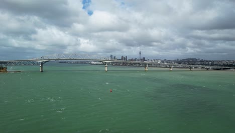 Auckland-Harbour-Bridge-Mit-Blick-Auf-Den-Türkisfarbenen-Hafen-Von-Waitemata-Und-Die-Skyline-Der-Innenstadt-Von-Einer-Luftdrohne-Aus,-Die-über-Das-Wasser-In-Neuseeland-Schwenkt