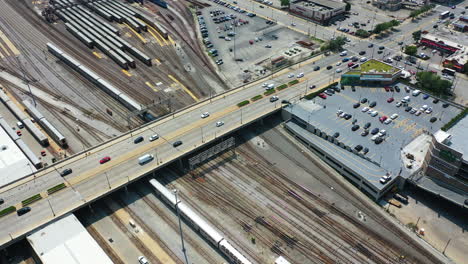 Vista-Aérea-Siguiendo-Un-Tren-Amtrak,-Conduciendo-Por-El-Soleado-Patio-De-Autos-De-Chicago