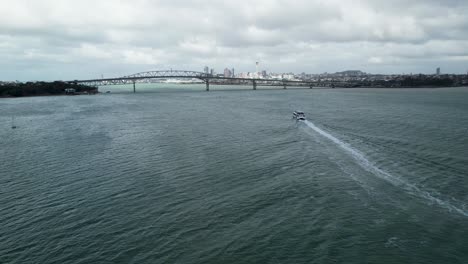 Aerial-Pull-Out-Shot-Over-the-Auckland-Waitemata-Harbour-with-a-Ferry-Boat-Heading-Towards-the-Auckland-Harbour-Bridge-with-City-Skyline-in-the-Background