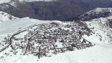 Aerial-view-establishing-the-mountain-village-of-Farellones-completely-snowed-in-on-a-sunny-day,-cusp-of-the-Andes-Mountains,-Chile